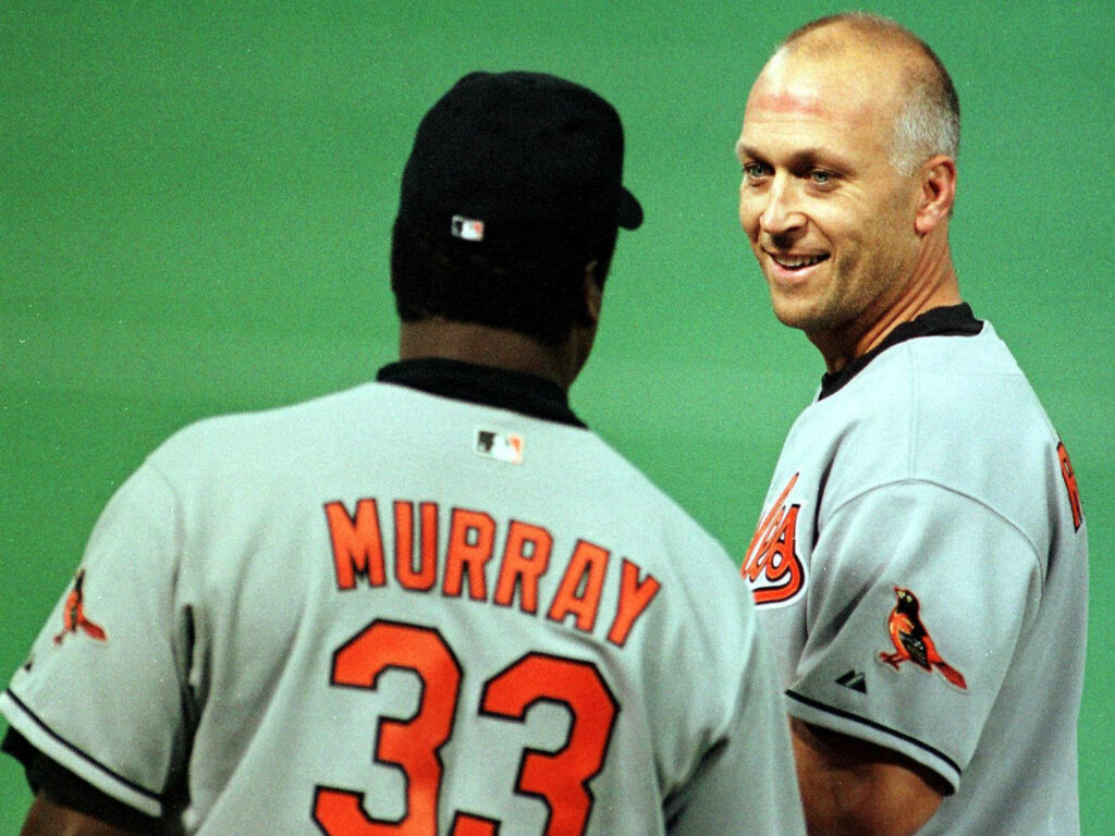 Cal Ripken Jr and Eddie Murray Orioles jerseys sharing candid baseball moment stadium background Wallpaper