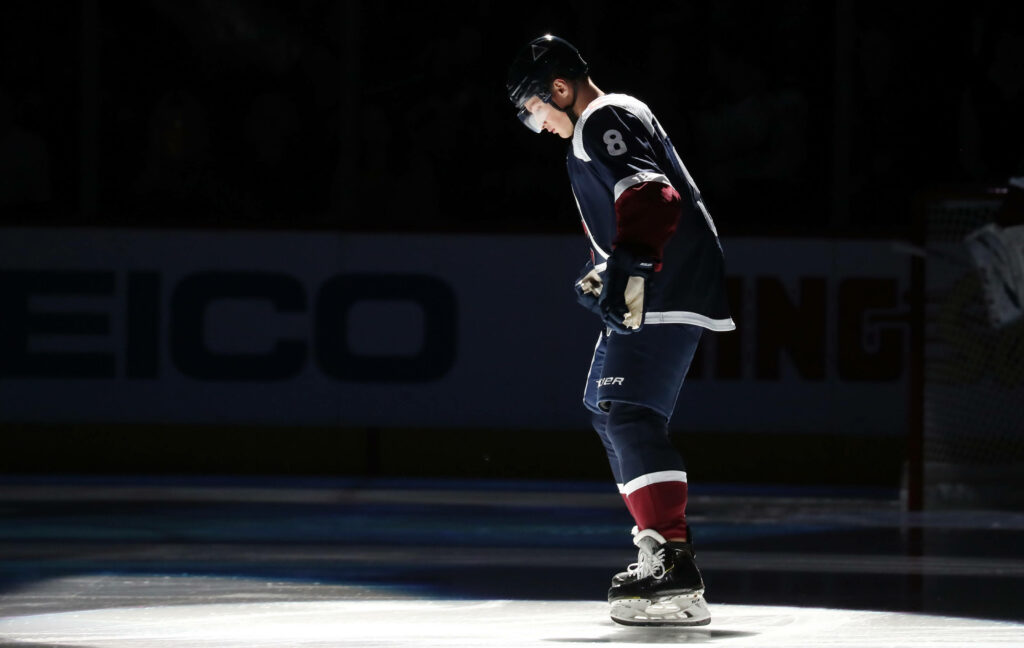 Cale Makar on ice under dark spotlight wearing navy and burgundy uniform intense hockey defenseman Wallpaper