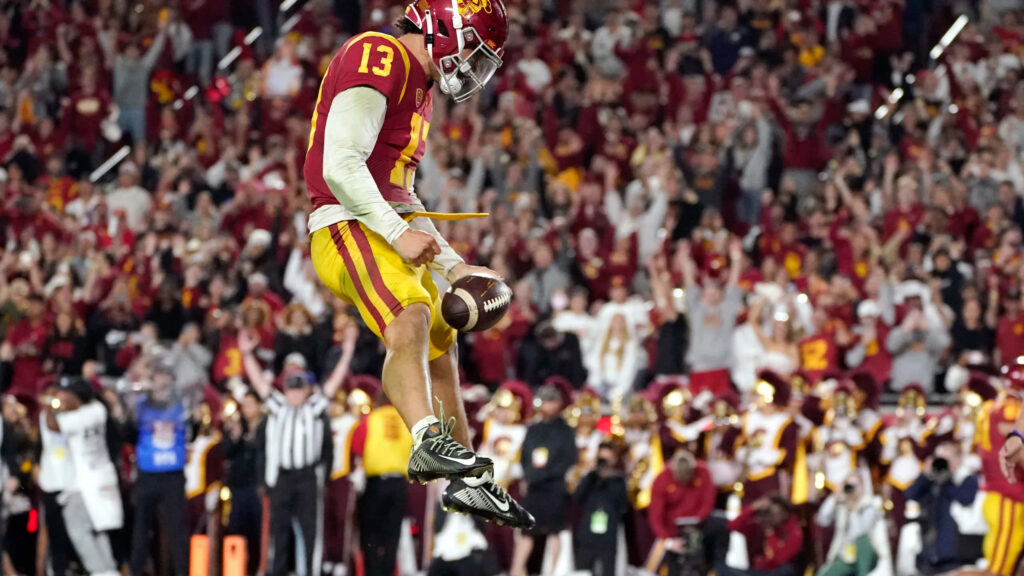 Caleb Williams leaping as football kicker in vibrant stadium with cheering team-colored crowd background Wallpaper