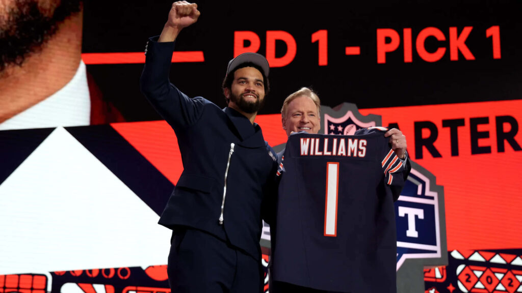 Caleb Williams celebrates NFL Draft first pick holding Chicago Bears jersey on red black stage Wallpaper