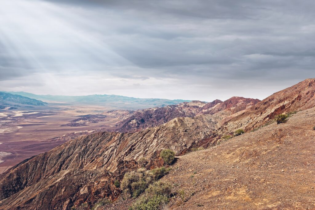California desert hills and mountains under dramatic clouds with sun rays illuminating rocks Wallpaper