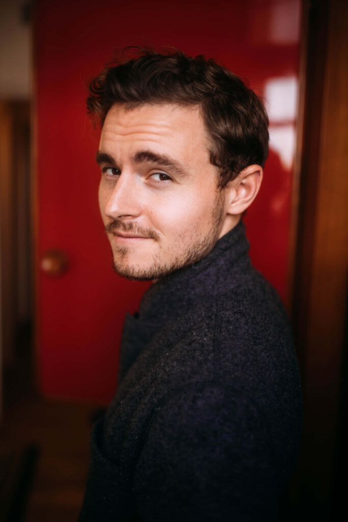 Callan McAuliffe candid portrait against bold red background with warm cinematic lighting and casual style Wallpaper