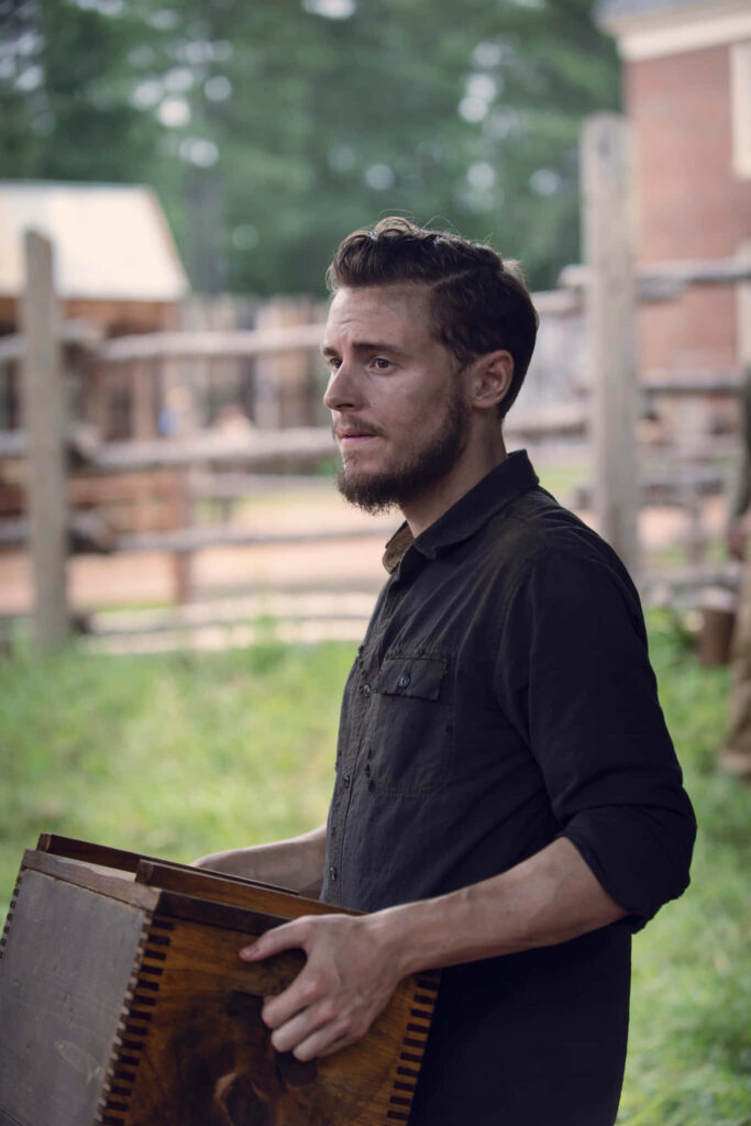 Callan McAuliffe outdoors holding wooden box in peaceful rustic setting with natural green tones Wallpaper