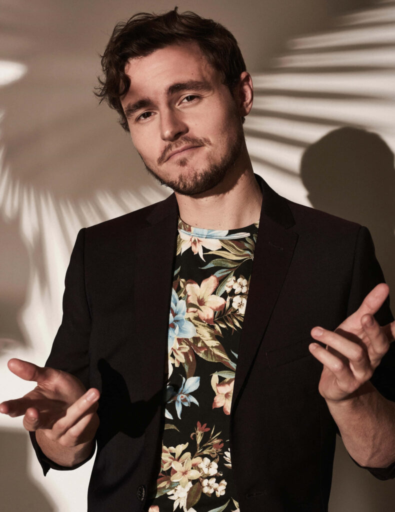 Callan McAuliffe stylish portrait in floral shirt and dark blazer with dramatic shadow background Wallpaper