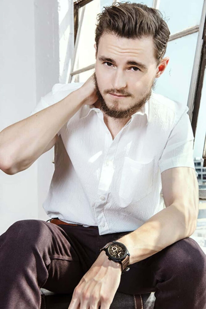 Callan McAuliffe in bright modern room wearing white shirt and dark trousers thoughtful pose Wallpaper
