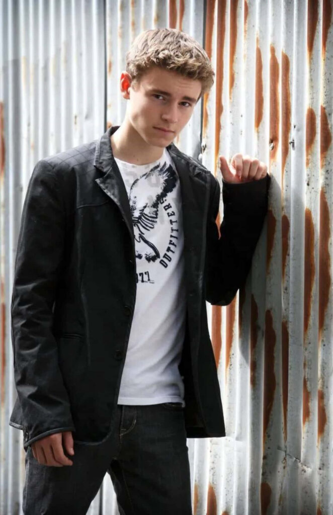 Callan McAuliffe in casual outfit against rustic corrugated metal wall urban portrait wallpaper