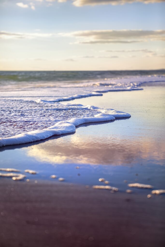 Calm beach with gentle sea foam pastel sky soft clouds and reflective wet sand wallpaper background