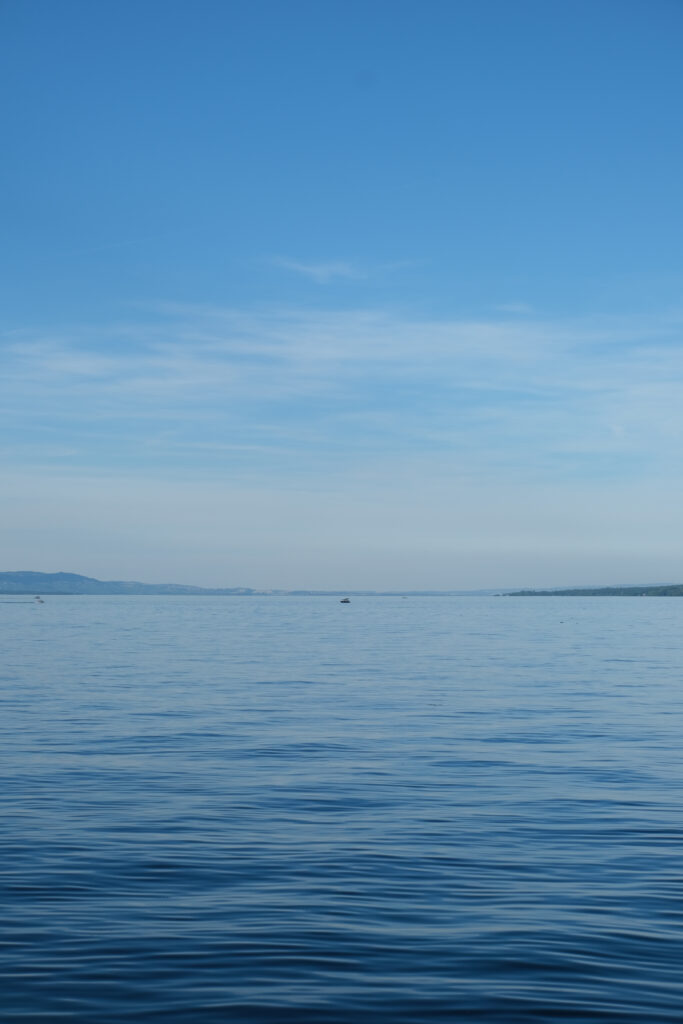 Serene blue sea wallpaper with calm ripples and distant boat under clear sky horizon background