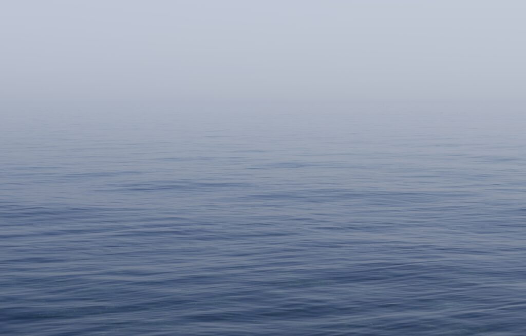 Calm sea with gentle blue ripples blending into pale sky minimalist serene nature wallpaper background