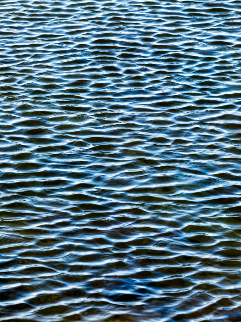 Sunlit water surface with gentle ripples natural glare blue and earthy tones calming fluid wallpaper background