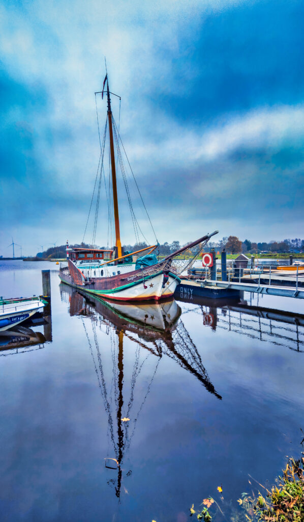 Classic sailboat at quiet river port with colorful hull and tall mast reflected in calm water Wallpaper