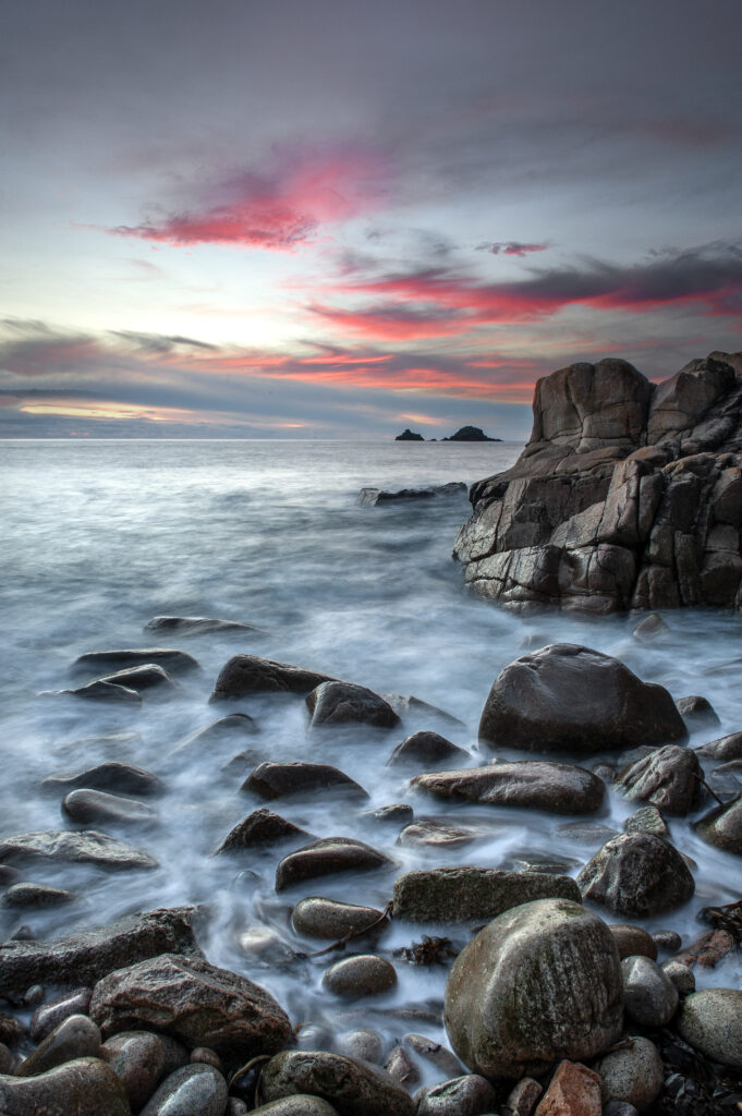 Serene coastal wallpaper with smooth rocks shoreline gentle waves dramatic pink blue gray sky