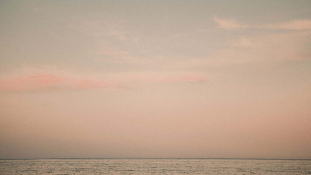 Calm ocean horizon at pastel sunset 4K wallpaper with soft peach and dusky sky tones