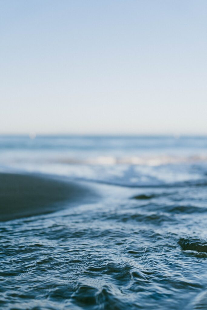 Close-up of gentle sea waves and ripples in soft blue hues with a calm ocean horizon wallpaper