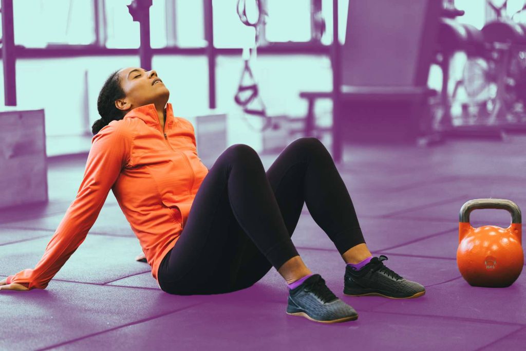 Woman in orange jacket resting on purple gym floor next to 20kg kettlebell post workout Wallpaper