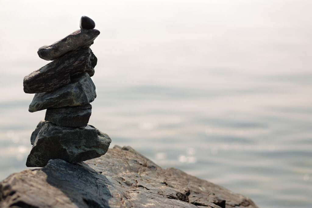Stacked balanced stones on rocky shore with calm sea backdrop serene minimalist wallpaper background