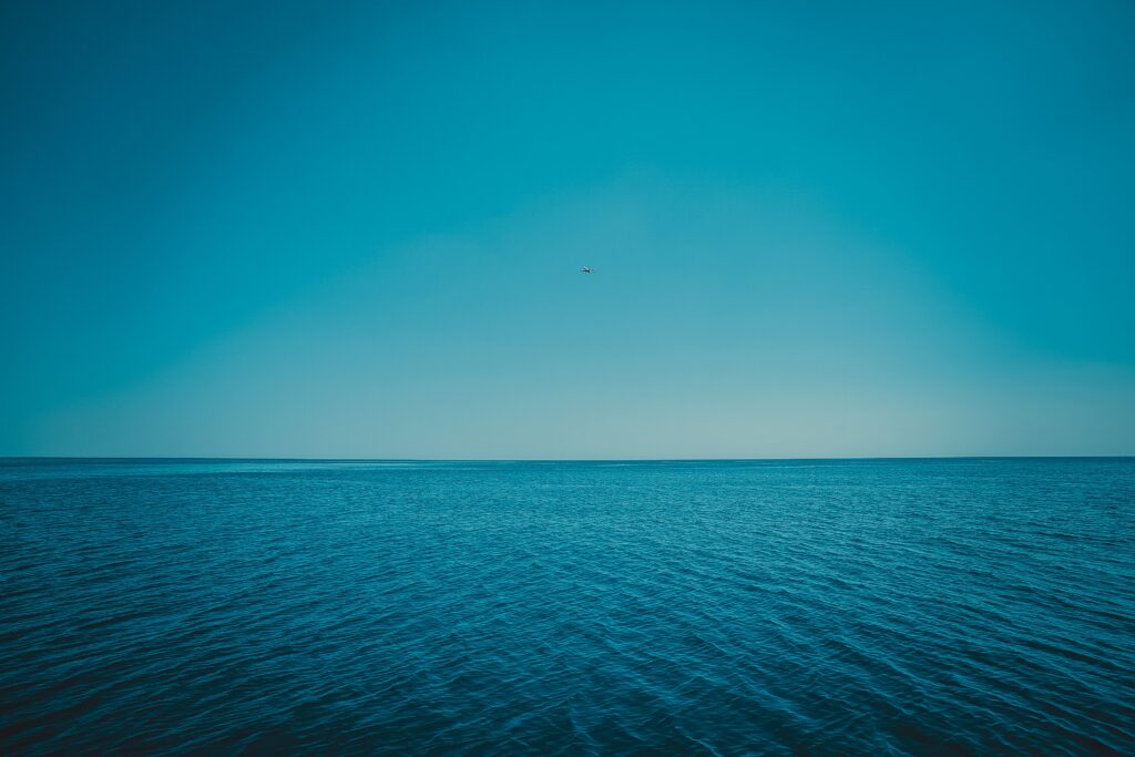 Calm sea with gentle ripples meeting clear horizon under expansive blue sky peaceful wallpaper