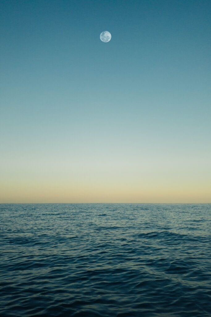 Calm sea at moonrise with clear sky reflecting blue and golden hues minimalist wallpaper background