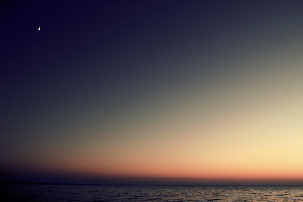 Serene sunset wallpaper with calm sea warm orange to deep blue sky and crescent moon background