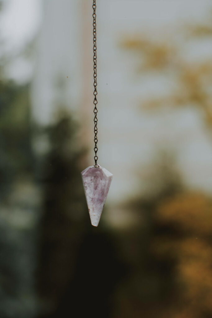 Delicate amethyst pendulum on fine chain against soft blurred outdoor background wallpaper