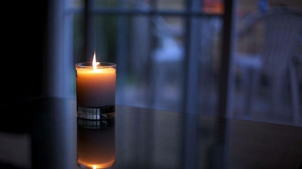 Soft glowing candle on reflective surface by balcony with warm light and cool blue tones background Wallpaper