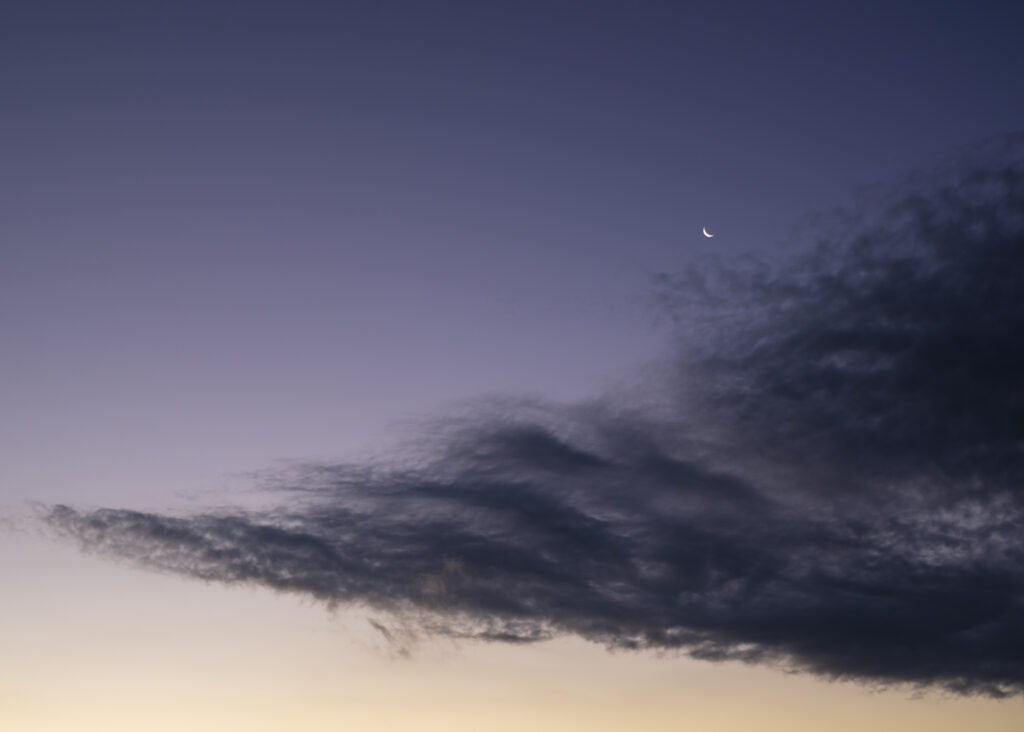 Crescent moon in purple and blue dusk sky with wispy clouds minimalist calming wallpaper background