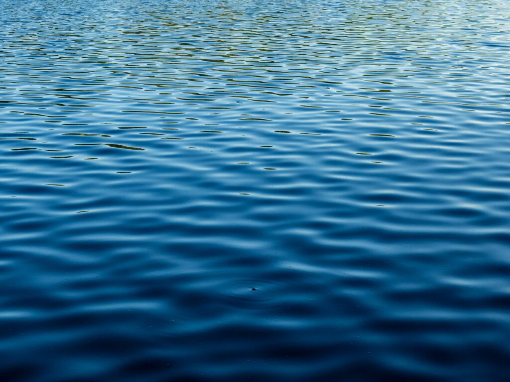 Calm deep blue water surface with gentle ripples and natural light reflections background wallpaper