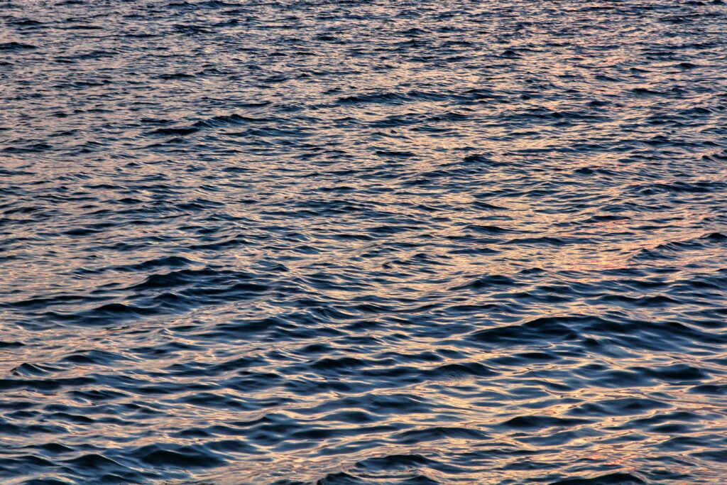 Wavy sea water wallpaper with golden sunlight reflections and calming blue orange ripples background