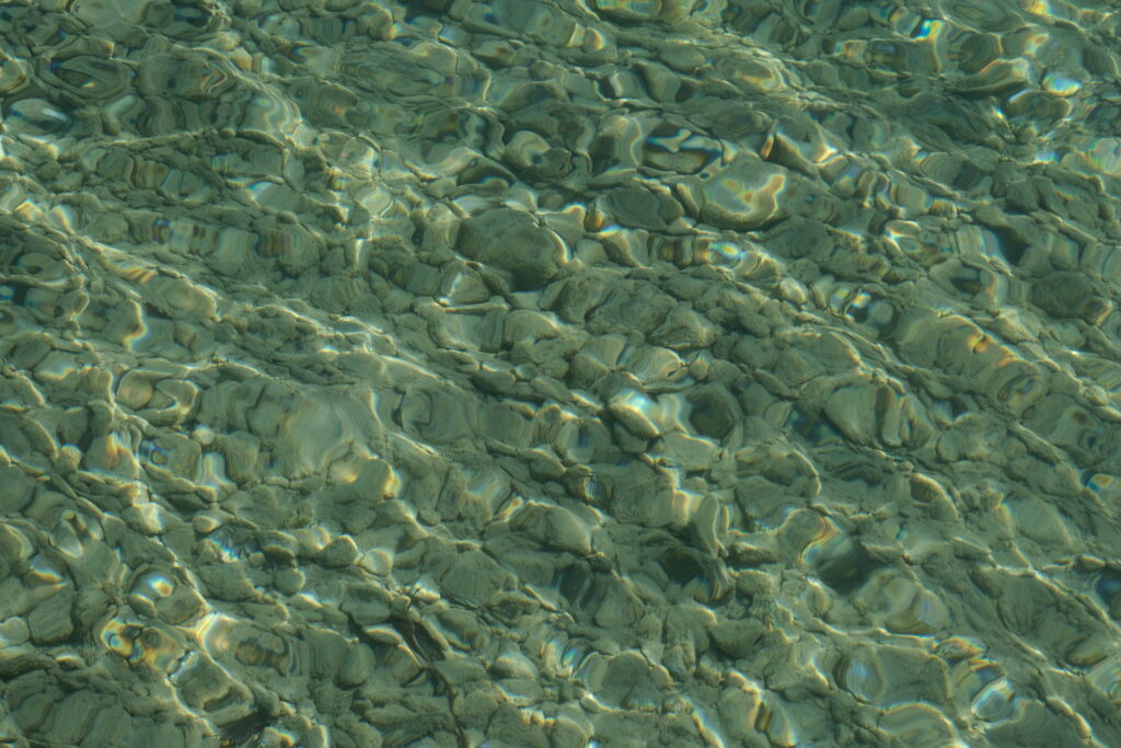 Minimalist wallpaper of smooth green and gray stones under clear water with sunlight ripples