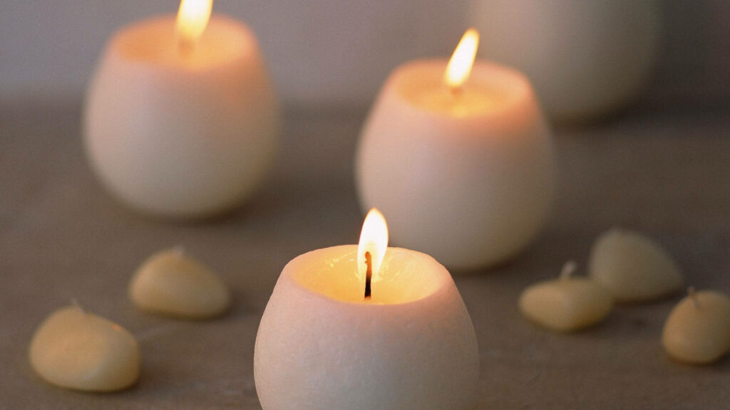 Three glowing white candles on beige background creating a calm minimalist relaxing wallpaper
