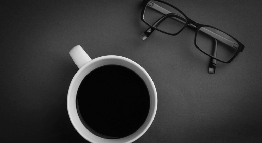 Steaming black coffee cup next to eyeglasses on dark surface minimal calming workspace background Wallpaper