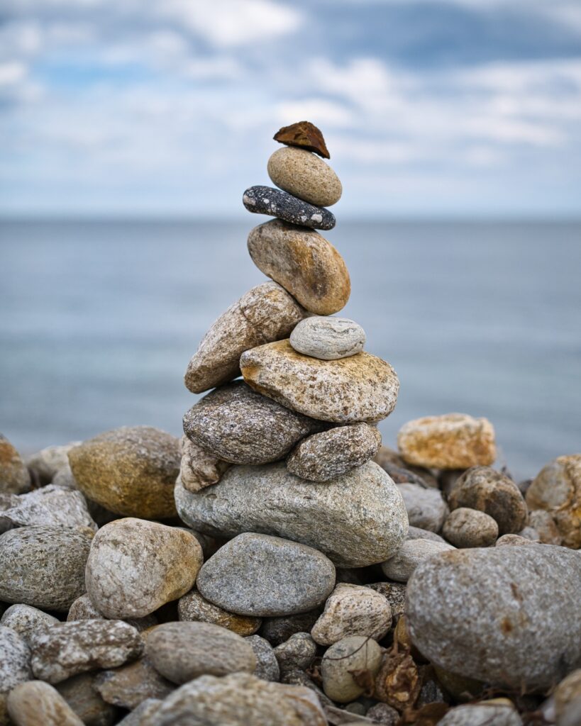 Stack of smooth stones balanced on rocky shore with blurred seascape and cloudy sky background Wallpaper
