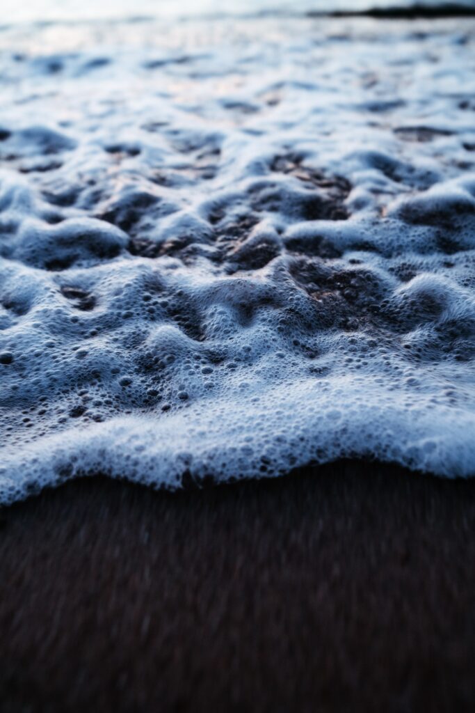 Close-up of ocean foam on dark sandy beach with textured surf in cool natural tones wallpaper