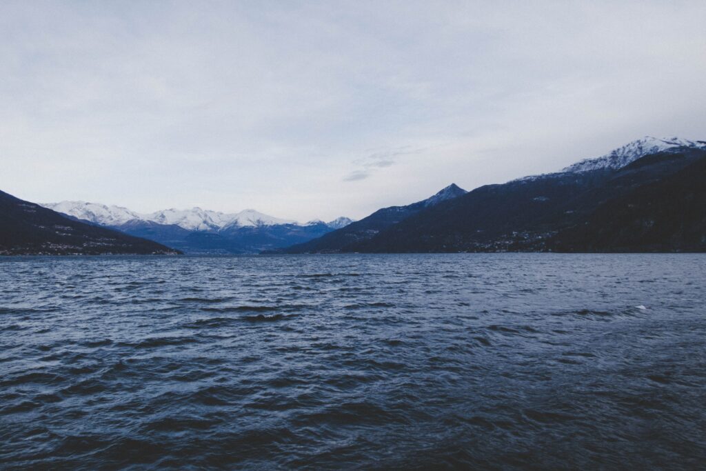 Serene sea with gentle ripples beneath muted blue sky framed by distant snow-capped mountains wallpaper