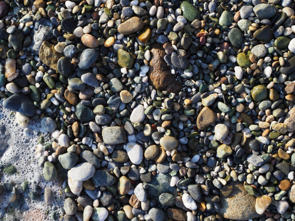 Smooth wet sea stones on shore with sunlight reflection natural calming textured wallpaper background