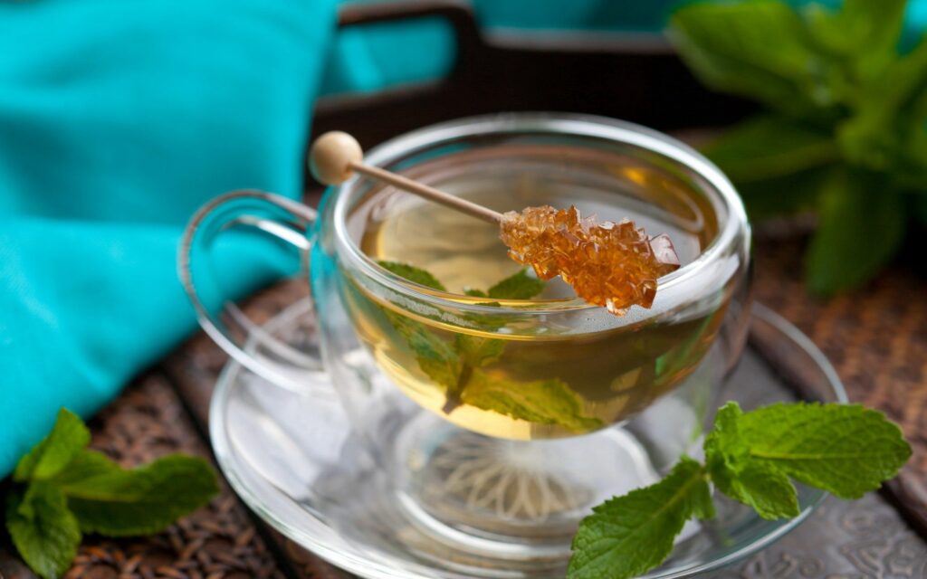 Calming Tea Wallpaper: Glass Cup, Green Leaves & Turquoise Background