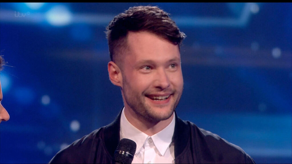 Calum Scott performing on Britains Got Talent stage wearing white shirt black jacket vibrant lights Wallpaper