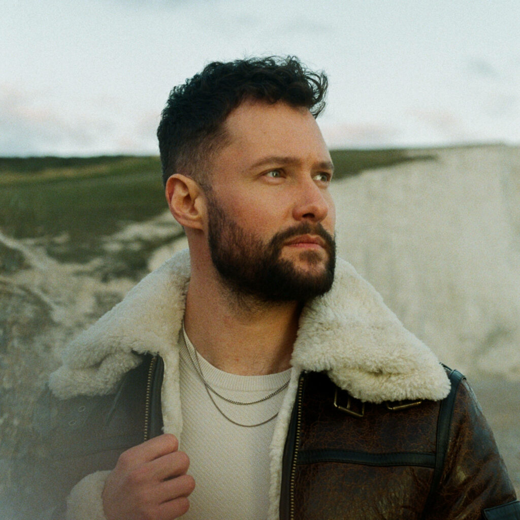 Calum Scott close-up profile with shearling jacket cliffs overcast sky serene natural wallpaper