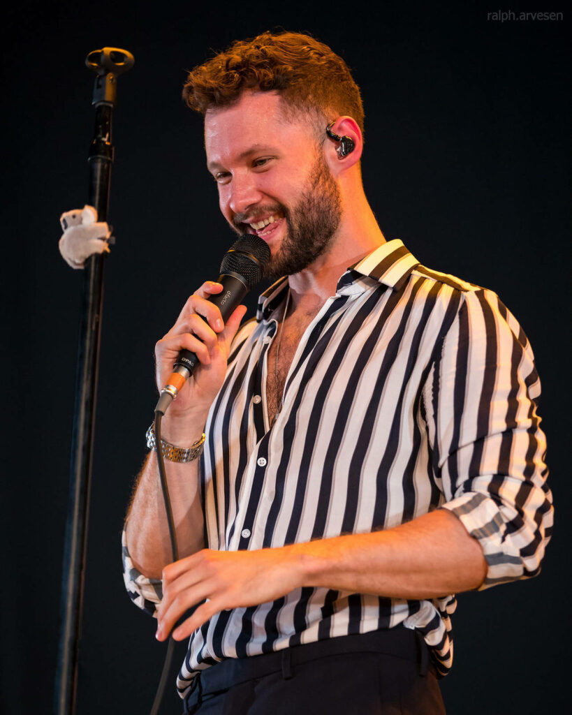 Calum Scott live concert performance smiling black white striped shirt dark stage background wallpaper