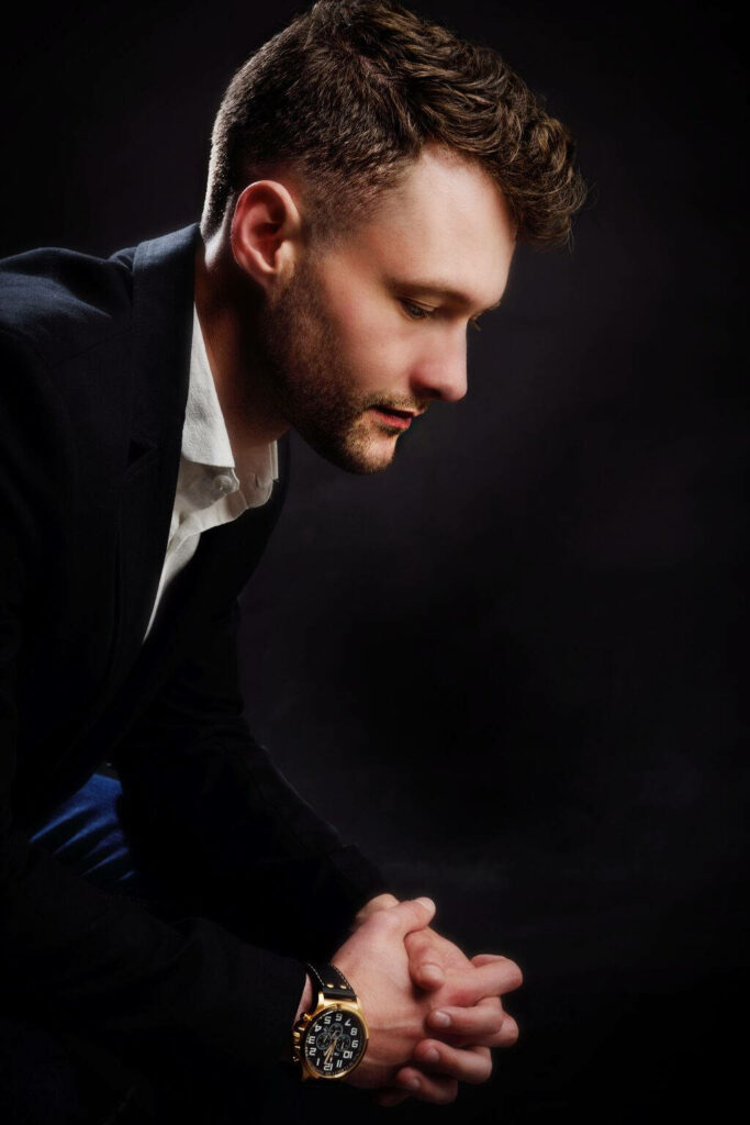Calum Scott portrait wallpaper thoughtful expression dark background formal attire elegant watch