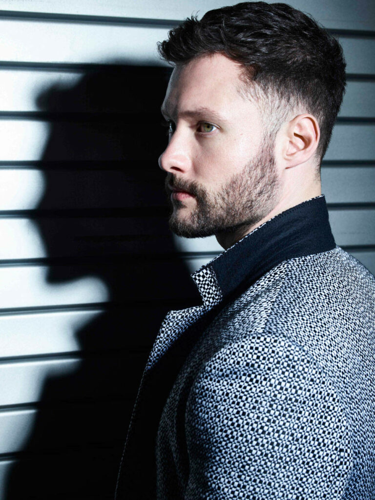Calum Scott side profile portrait with metallic striped background and textured patterned jacket Wallpaper