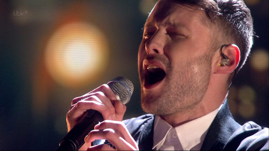 Calum Scott singing passionately on stage during Britains Got Talent with dramatic warm lighting Wallpaper