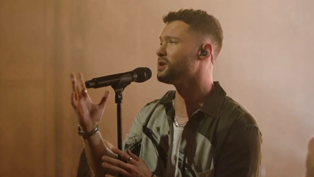Calum Scott passionately singing on stage under warm lighting with expressive gestures and style Wallpaper