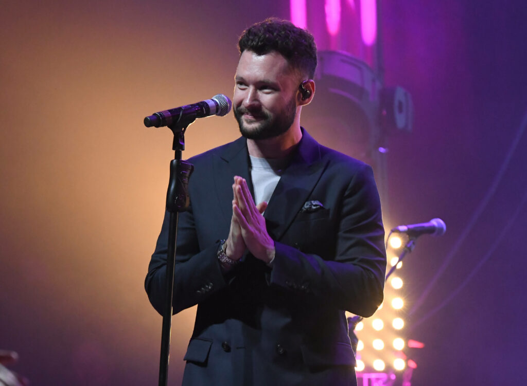 Calum Scott performing live on stage with warm spotlights and vibrant purple concert lighting Wallpaper