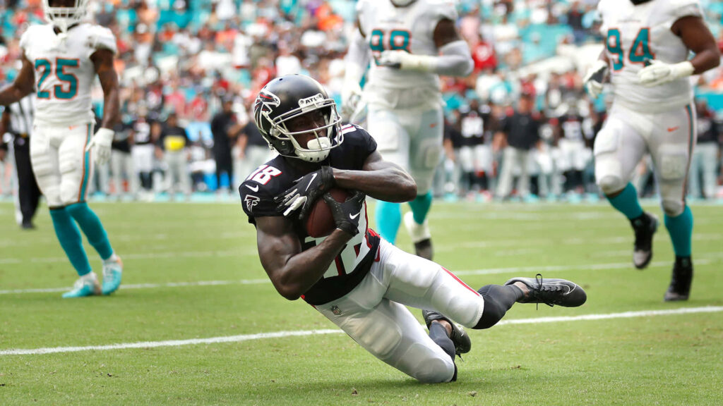 Calvin Ridley catching football in black Atlanta Falcons uniform on vibrant green field during game Wallpaper