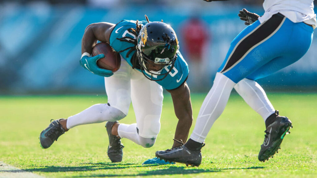 Calvin Ridley pushing forward gripping football in teal and white uniform intense action shot Wallpaper
