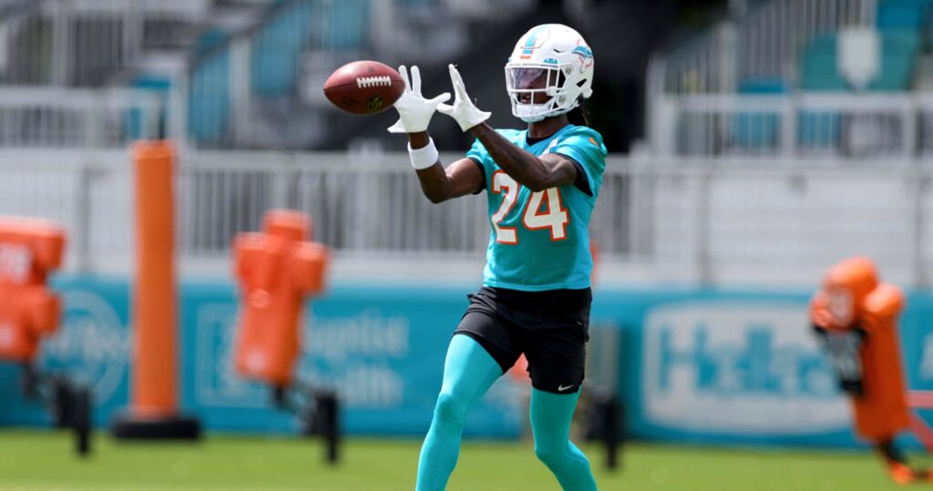 Cam Smith in teal Miami Dolphins uniform number 24 catches football on sunlit training field Wallpaper