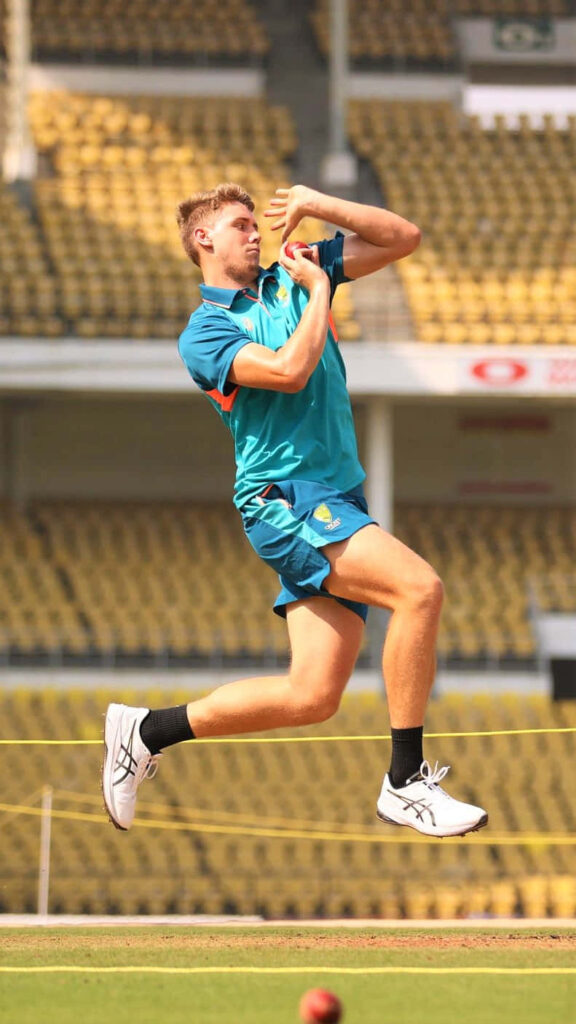 Cameron Green delivering fast ball in Australian cricket kit on sunlit stadium field with yellow seats Wallpaper