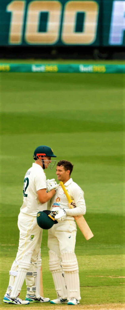 Cameron Green in cricket whites holding bat on green pitch with mist and blurred scoreboard background Wallpaper