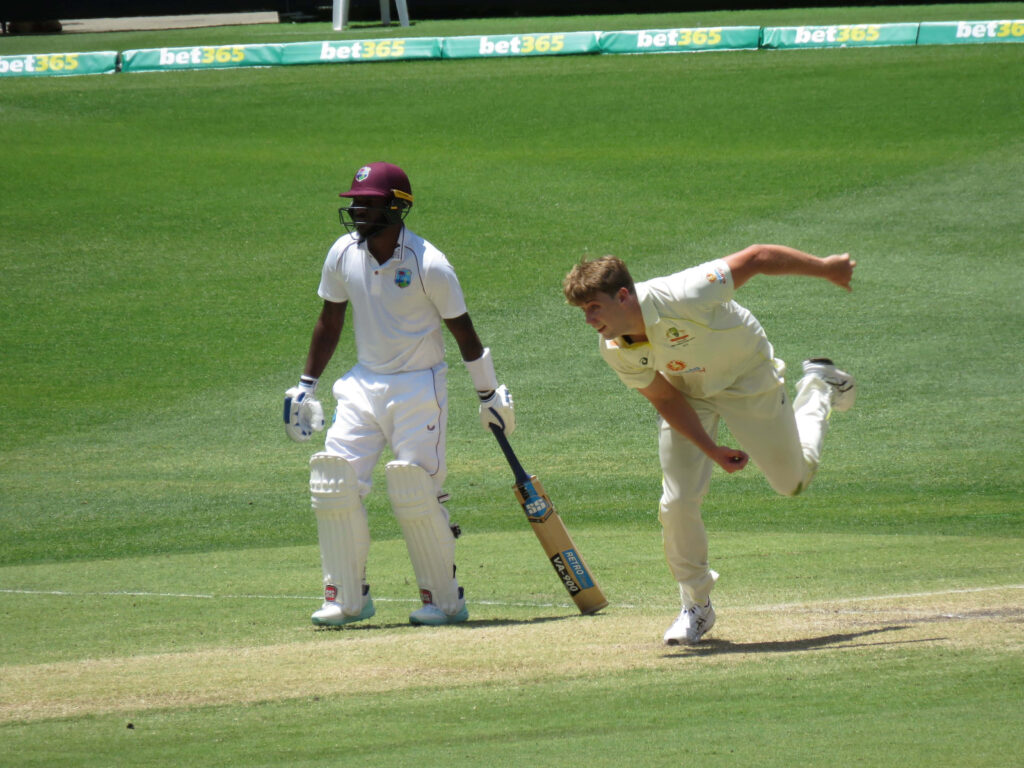 Cameron Green bowling powerfully on vibrant green cricket field under clear blue skies during match Wallpaper